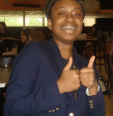 Людина в темно-синьому блейзері, яка показує два великі пальці вгору в приміщенні кафетерію.